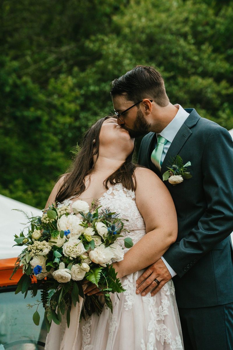Ashley and Anthony share a kiss while holding their bouquet beside the orange truck