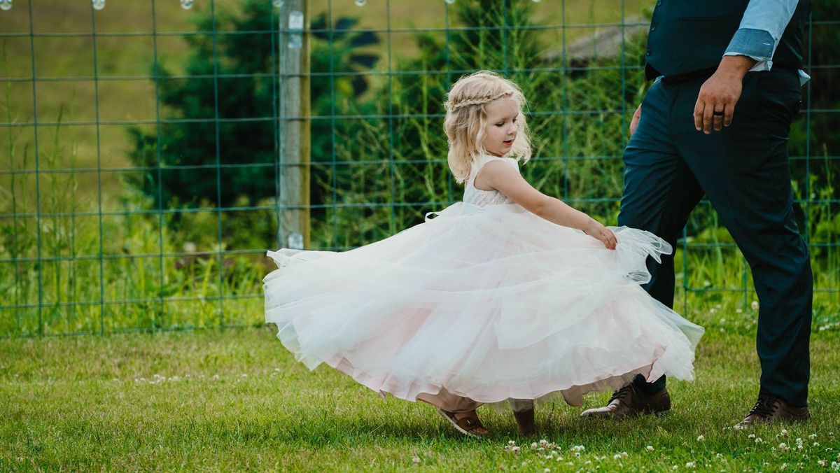 A child twirls in a white dress on the lawn