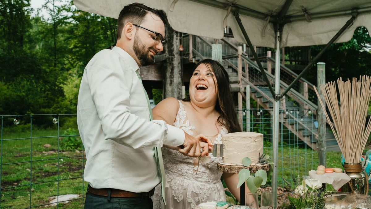 Ashley and Anthony laugh together while cutting their wedding cake