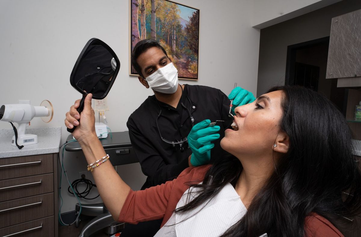 BPS Periodontics staff member in scrubs beside a person in a dental chair holding a mirror