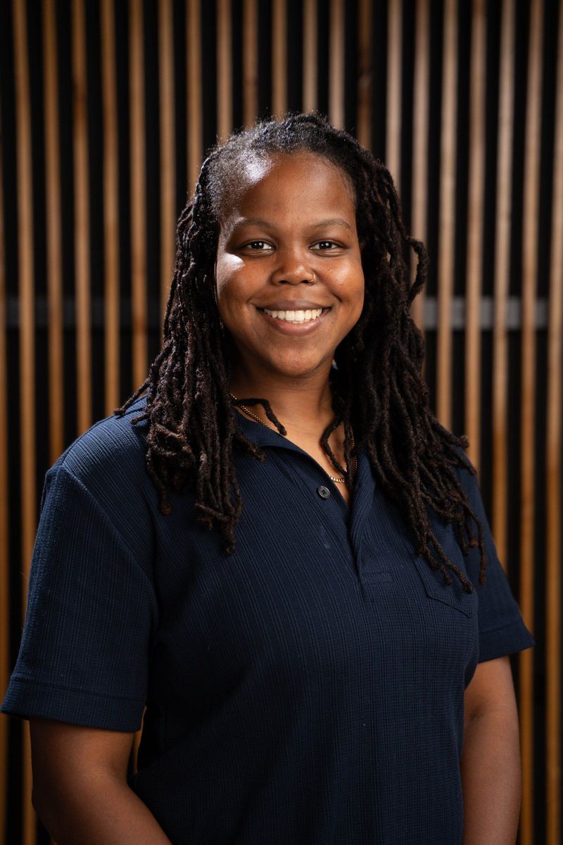 Smiling Brooke Team member in a navy polo shirt before the wood-slat background