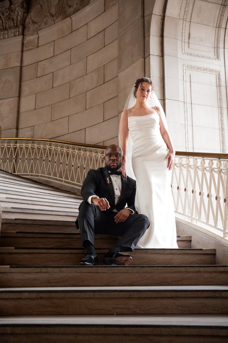 Christina stands beside the window while Tajay sits on a stair below her