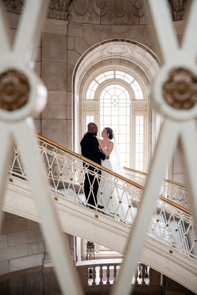 Christina and Tajay framed by an arched window and an ornate stair railing