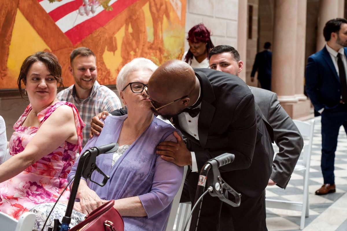 Tajay leans down to greet a seated loved one with a kiss
