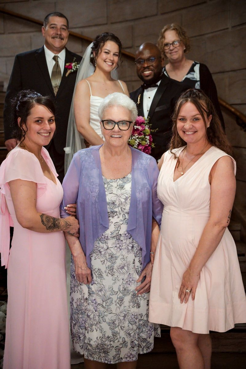 A group of loved ones gathers around Christina on the staircase