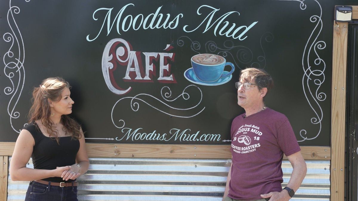 Elise interviews a guest beside the Moodus Mud Café sign