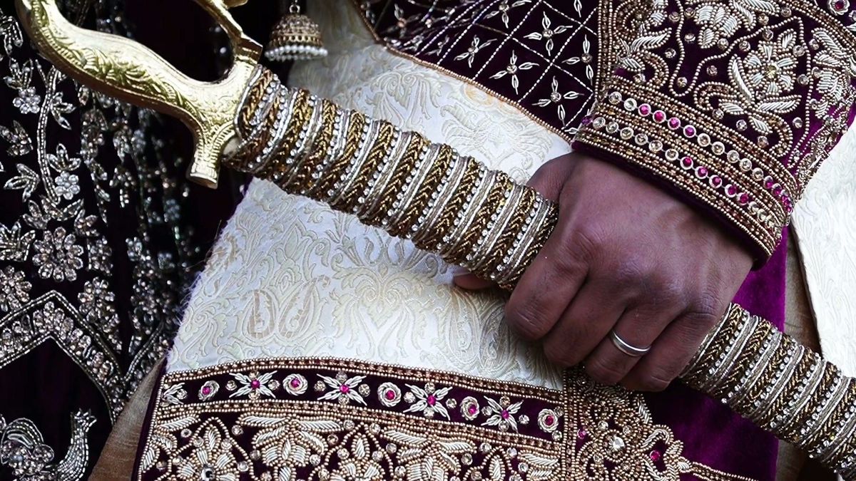 A close detail of embroidered attire and an ornate sword handle — video frame