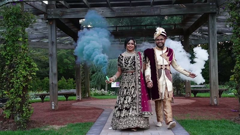 The couple smile beneath a wooden pergola with blue and white smoke around them — video frame