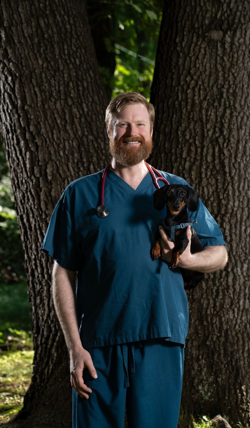 Farmington Animal Hospital portrait of a man in scrubs holding a small black dog outdoors