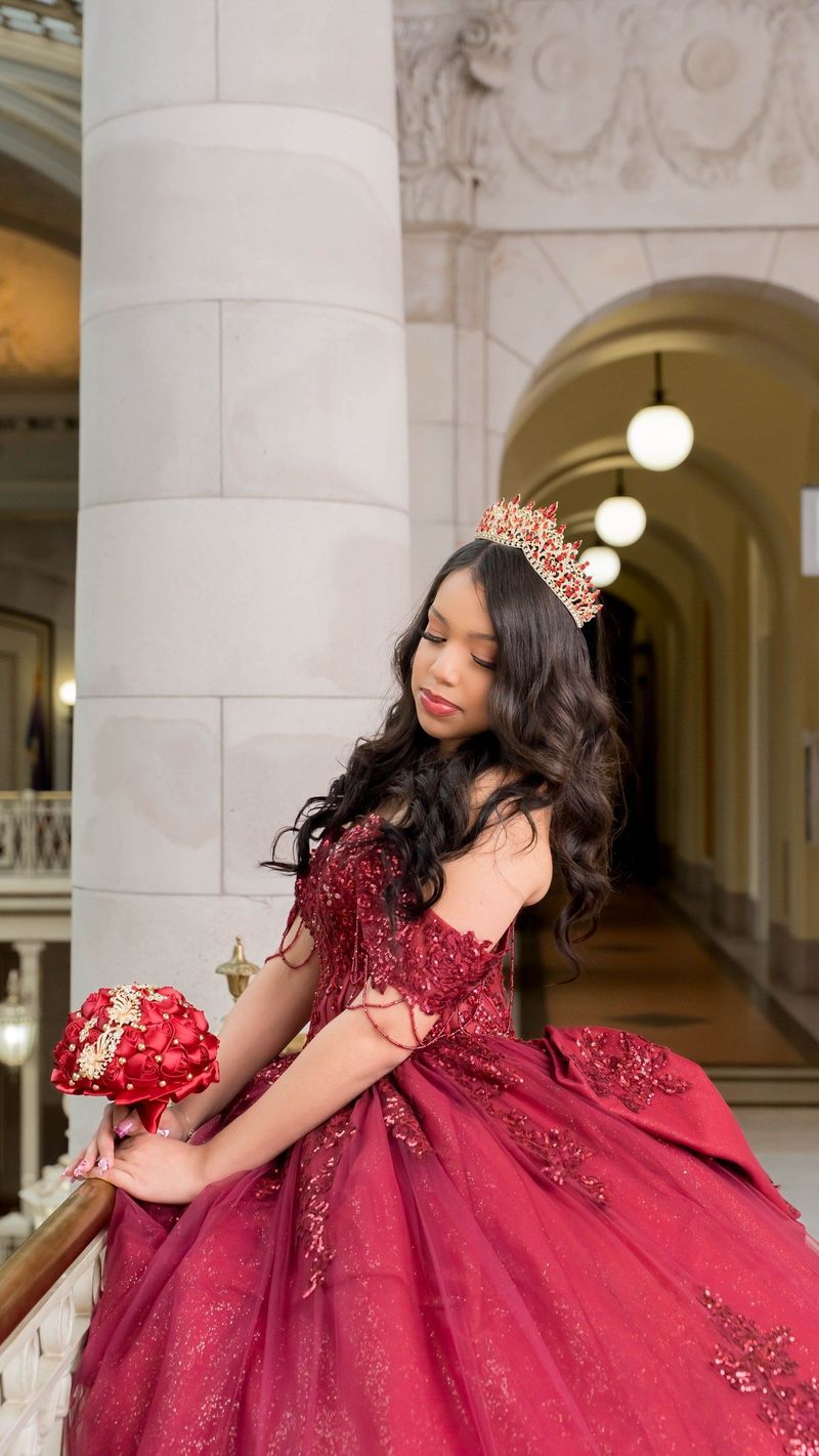 Genesis looks over her shoulder beside a column with her red bouquet
