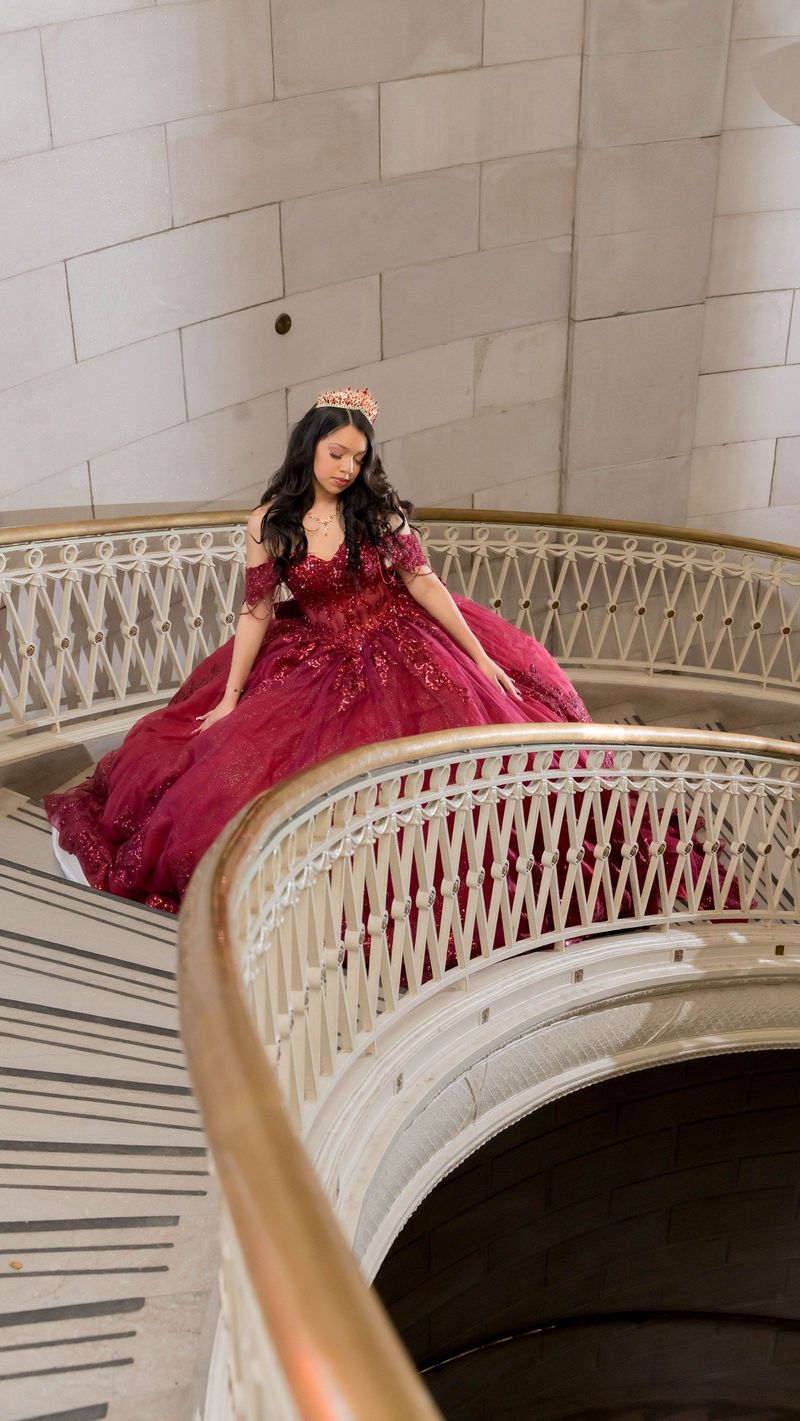 The staircase curves around Genesis and her full burgundy skirt