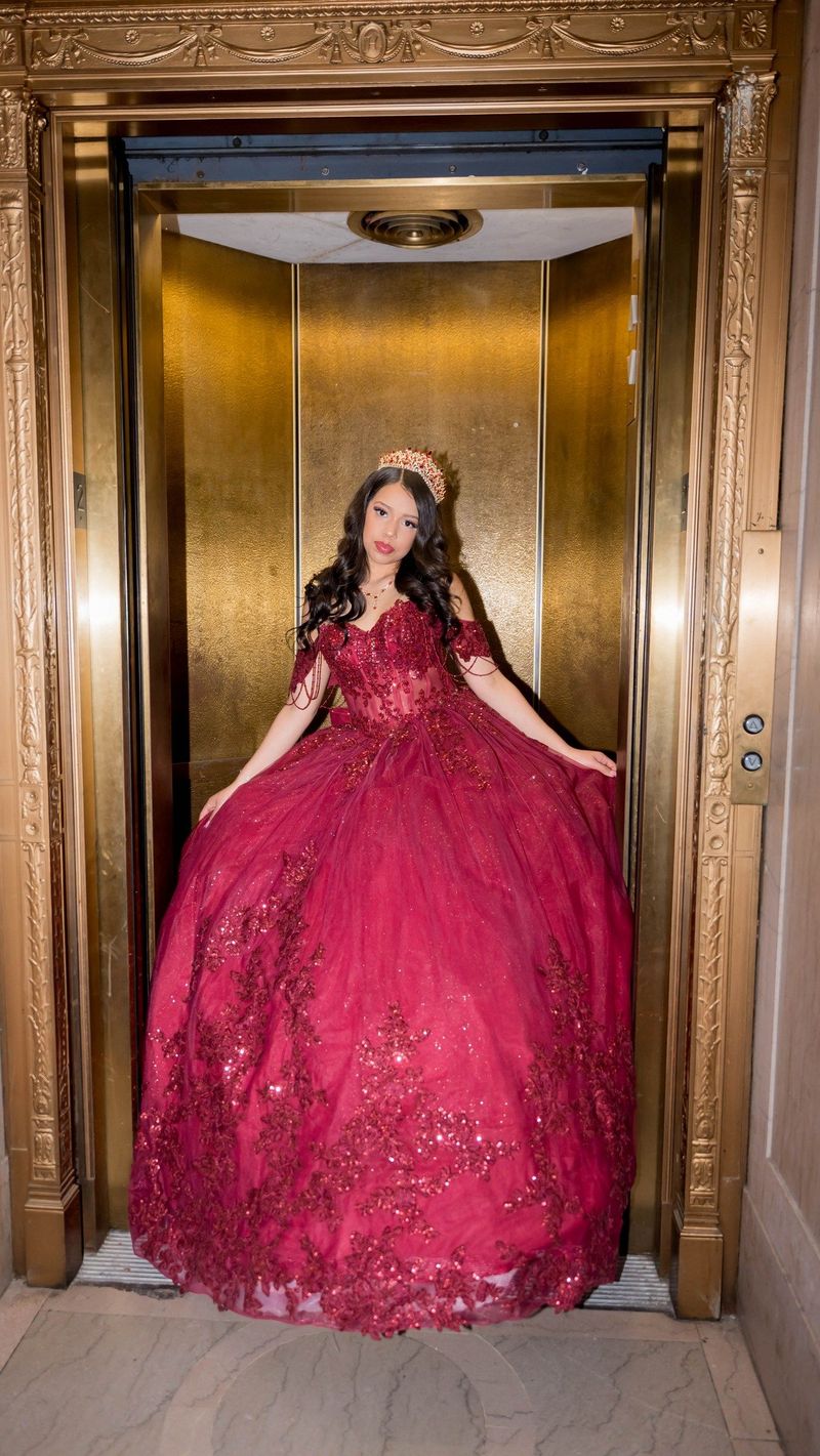 The golden elevator doorway frames Genesis and her burgundy gown