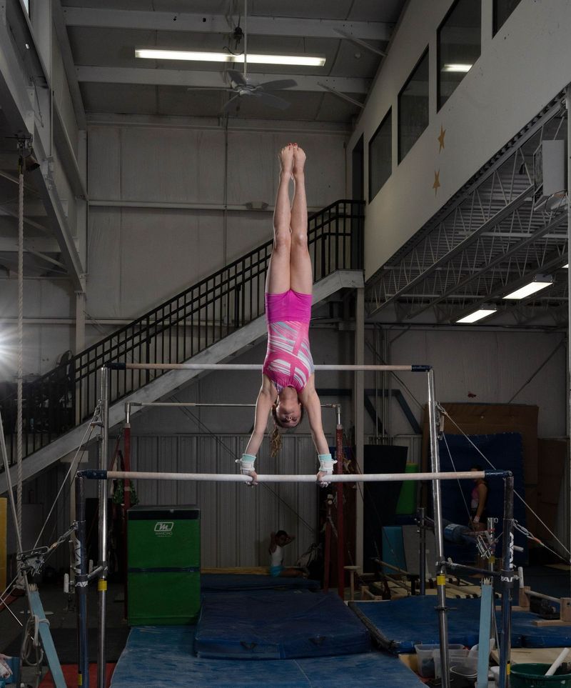A gymnast in a pink leotard holding a handstand on the uneven bars inside the Gymnastics Training Center gym