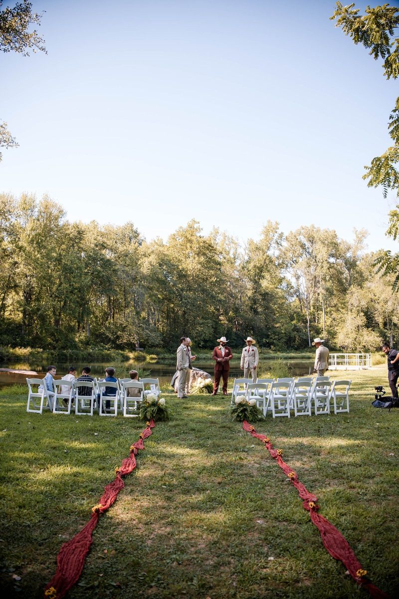 A red fabric aisle leads between white ceremony chairs toward the wooded pond