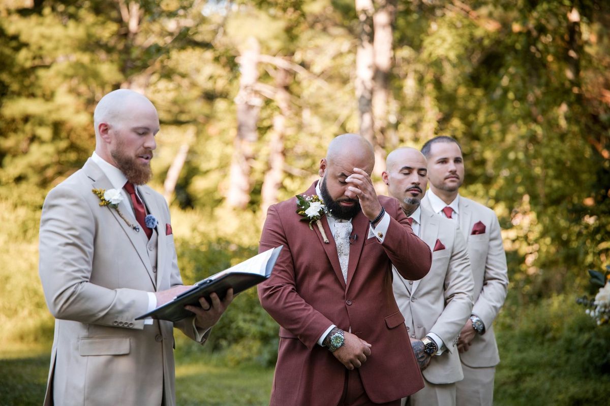Jacob lifts a hand toward his eye while standing beside the officiant