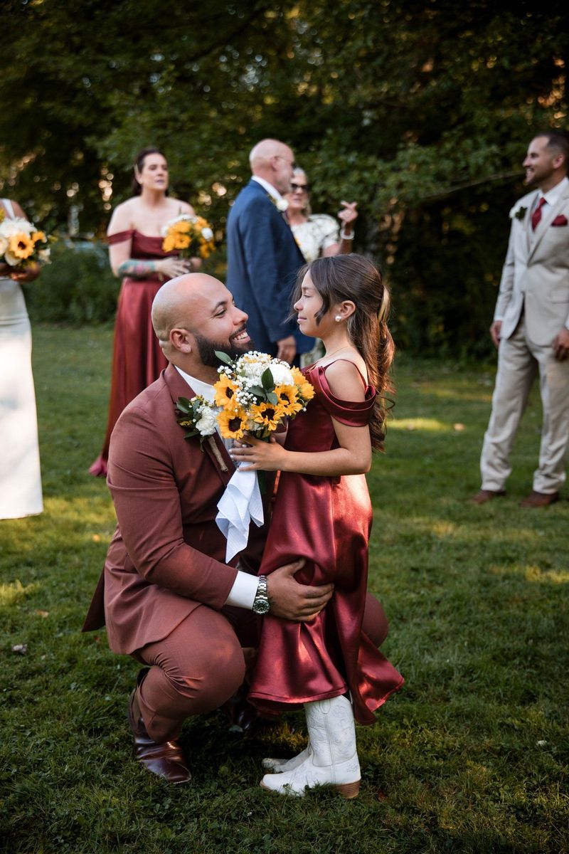 Jacob kneels beside a young wedding party member holding flowers