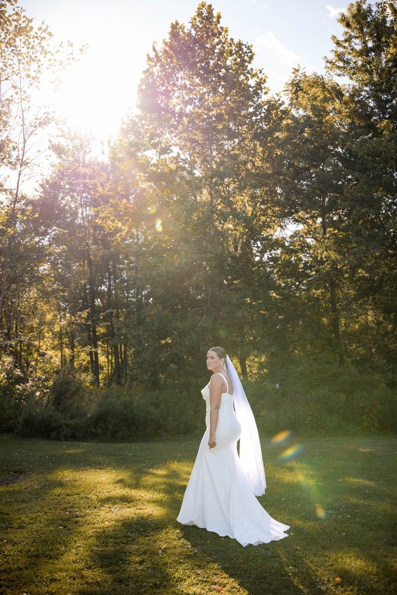 Thea stands on the lawn with sunlight filtering through the trees behind her