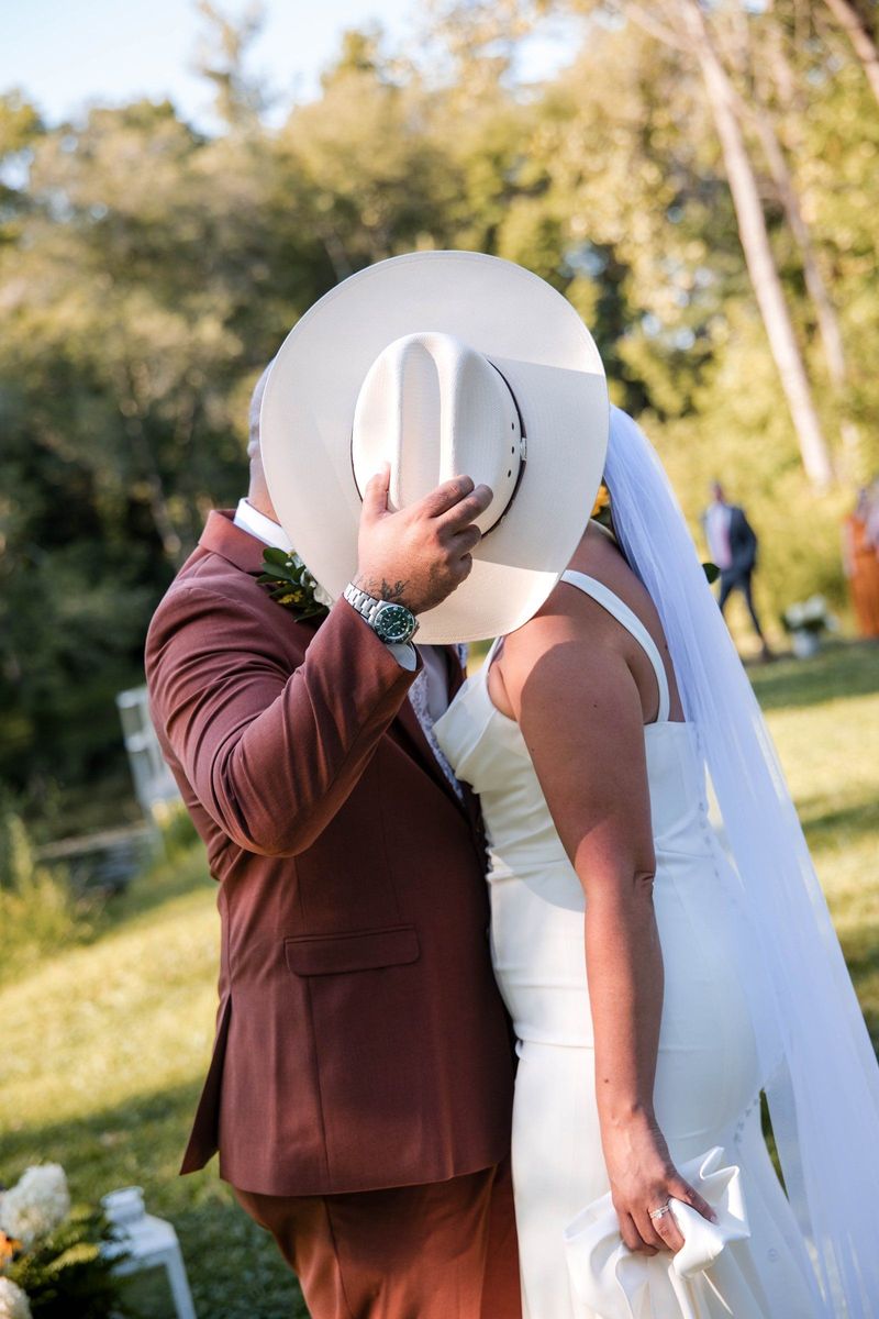 Jacob and Thea kiss behind the brim of a white cowboy hat