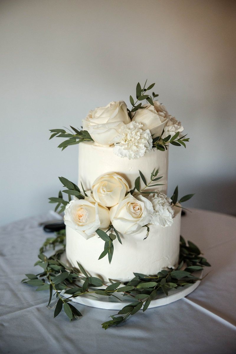A white tiered wedding cake decorated with white flowers and greenery
