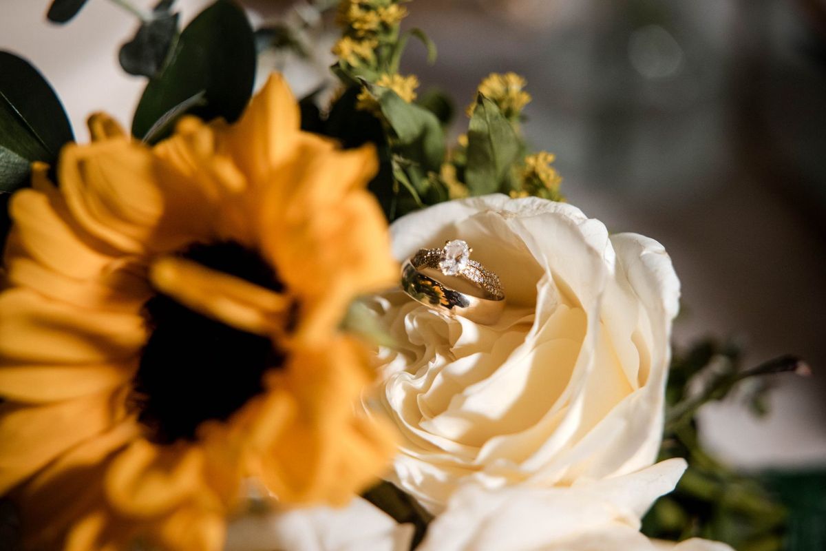 Wedding rings nestled among white roses and a sunflower