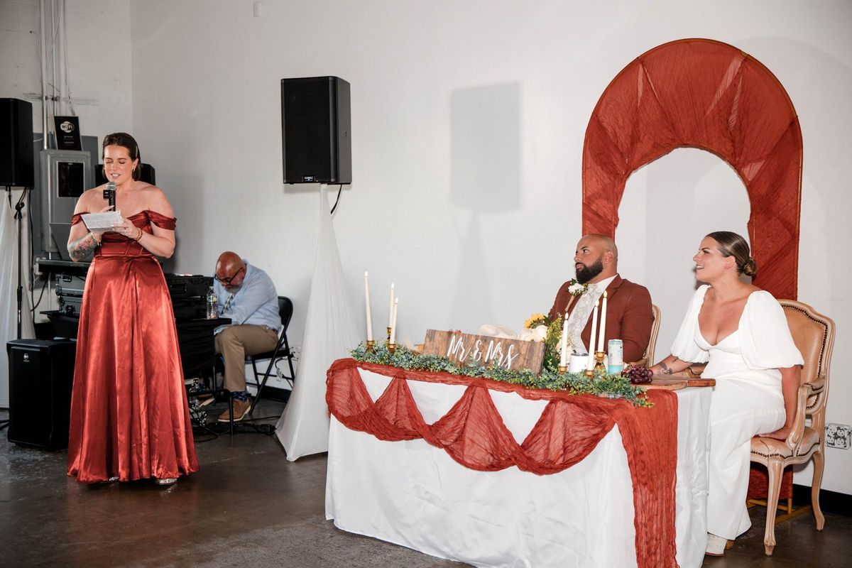 A speaker in a rust-colored dress reads beside the sweetheart table