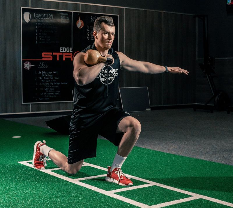 Athlete mid-lunge holding a kettlebell on an indoor training turf