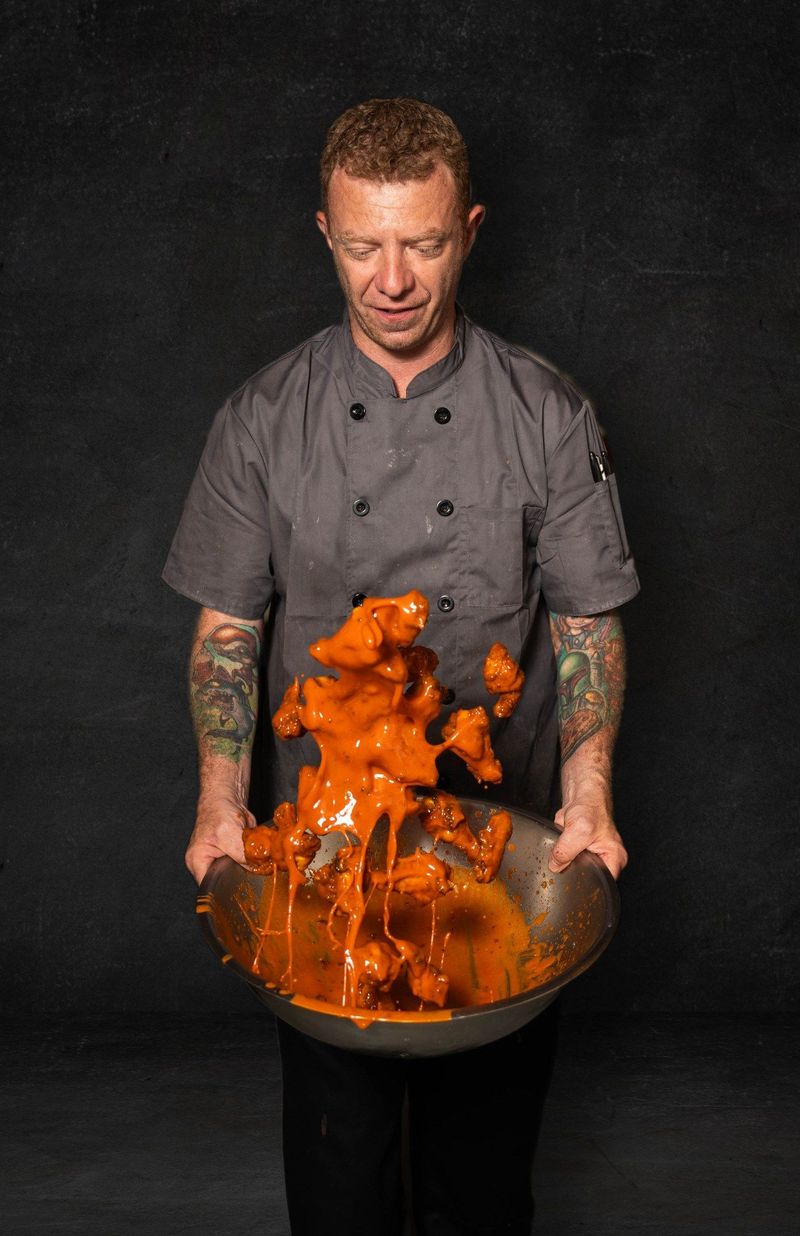 A Luna's Pizza chef tosses food in bright orange sauce above a metal mixing bowl against a dark background