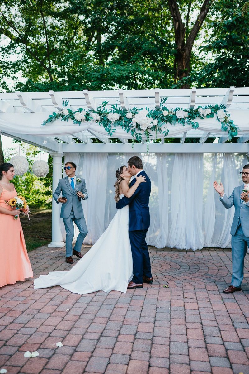 Mariana and Max kissing beneath the outdoor ceremony arbor