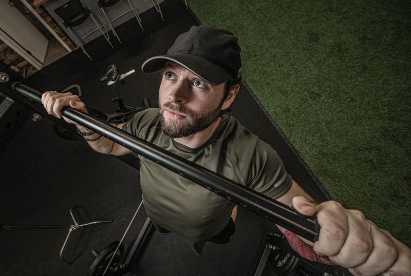 A man in a cap gripping a barbell, photographed from above in a gym
