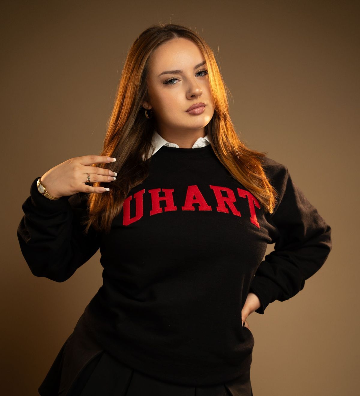 Studio portrait of a woman in a black university sweatshirt against a warm tan backdrop