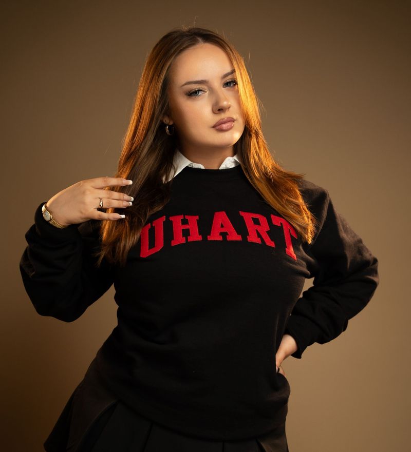 Studio portrait of a woman in a black university sweatshirt against a warm tan backdrop