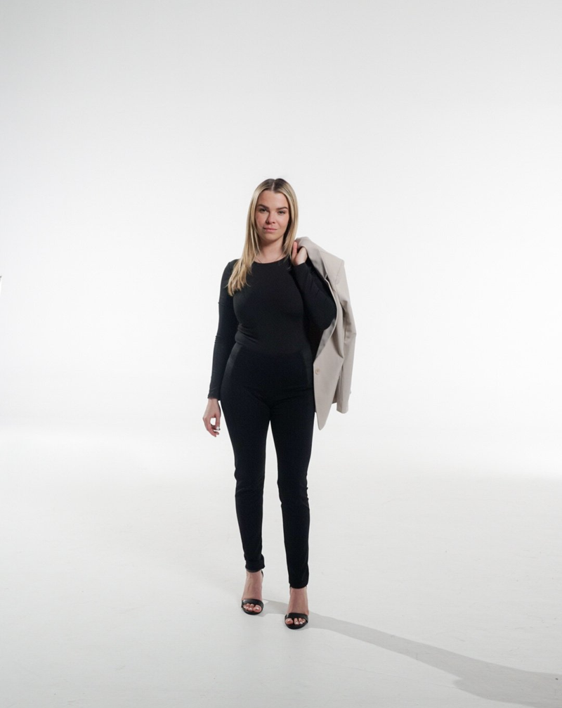 A woman standing on a white studio backdrop with a blazer over her shoulder