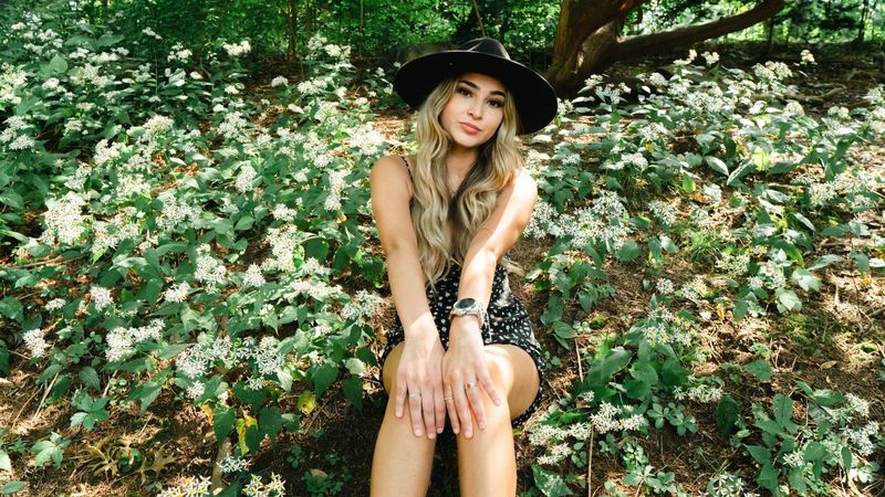 A woman in a black wide-brim hat sitting among white wildflowers in the woods