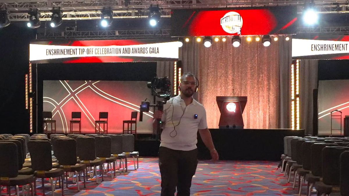A videographer with a camera on a handheld stabilizer walking through the Basketball Hall of Fame enshrinement gala ballroom