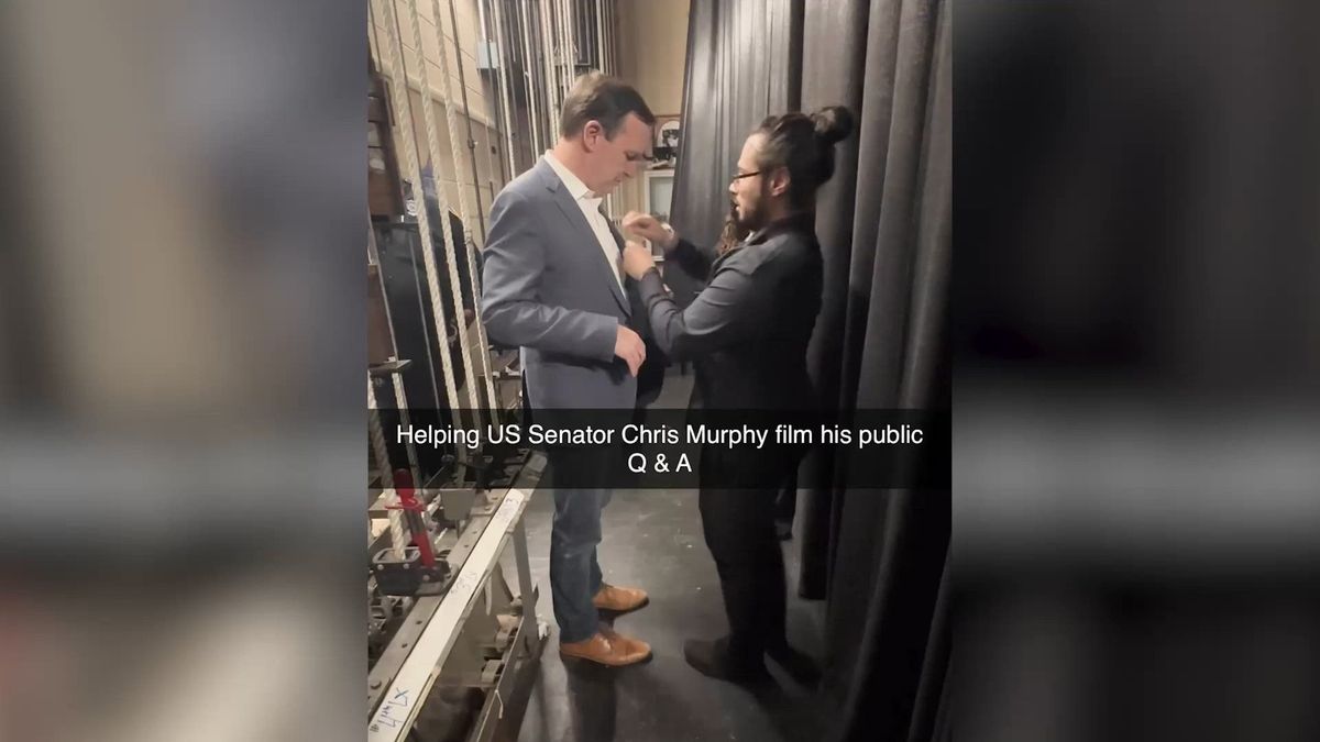 A Legend Photo & Film crew member adjusting the jacket of U.S. Senator Chris Murphy backstage before a public Q&A