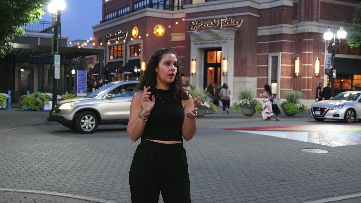 Robyn presents beside a restaurant-lined street in the evening