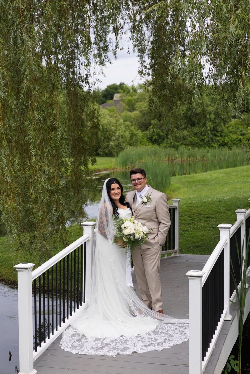 Sadie and Mat stand together on the bridge with her lace train spread out