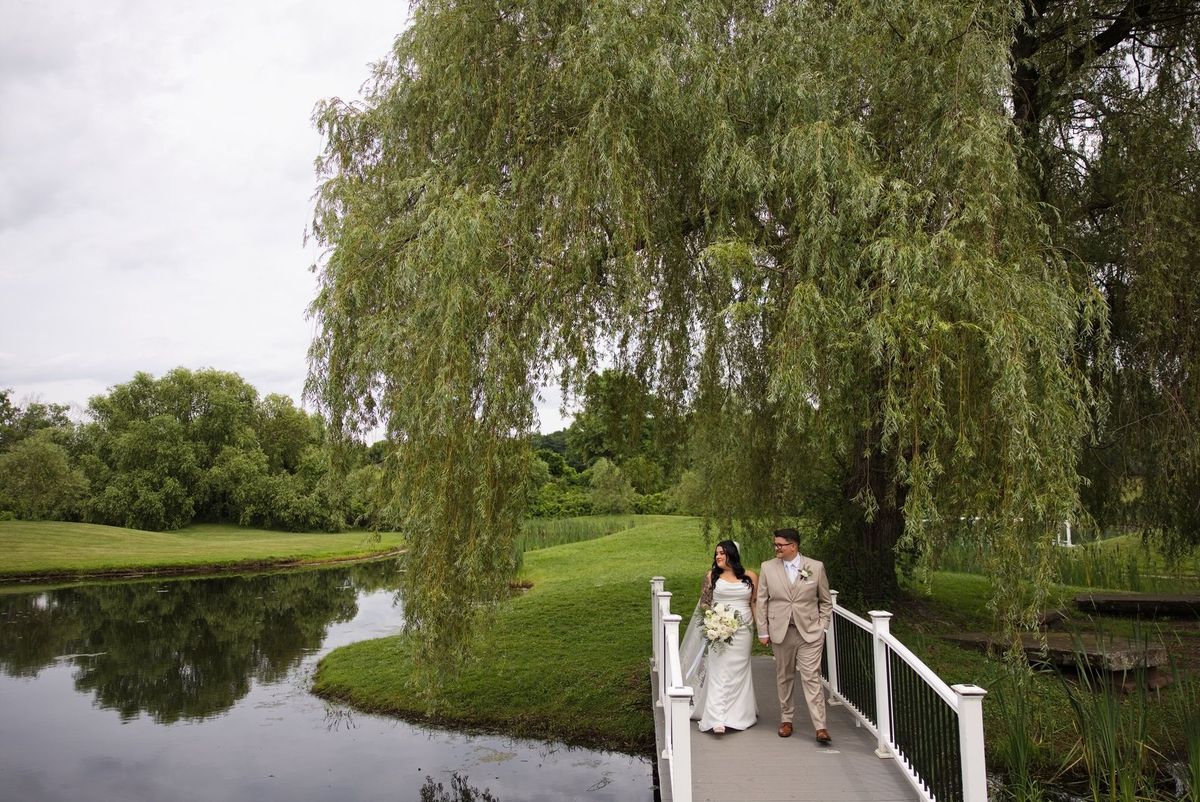 A wide portrait of Sadie and Mat seated on the bridge beside the pond