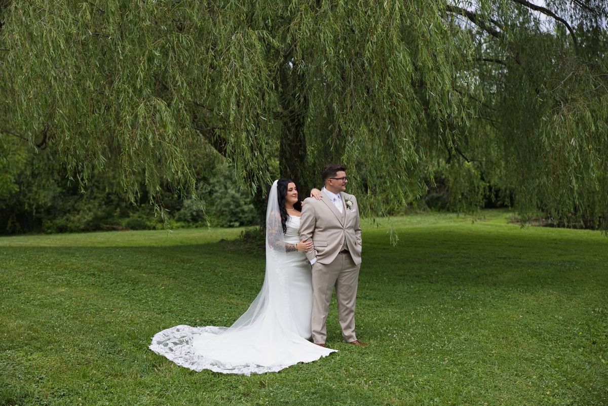 Sadie and Mat beneath the willow trees with her train spread across the lawn