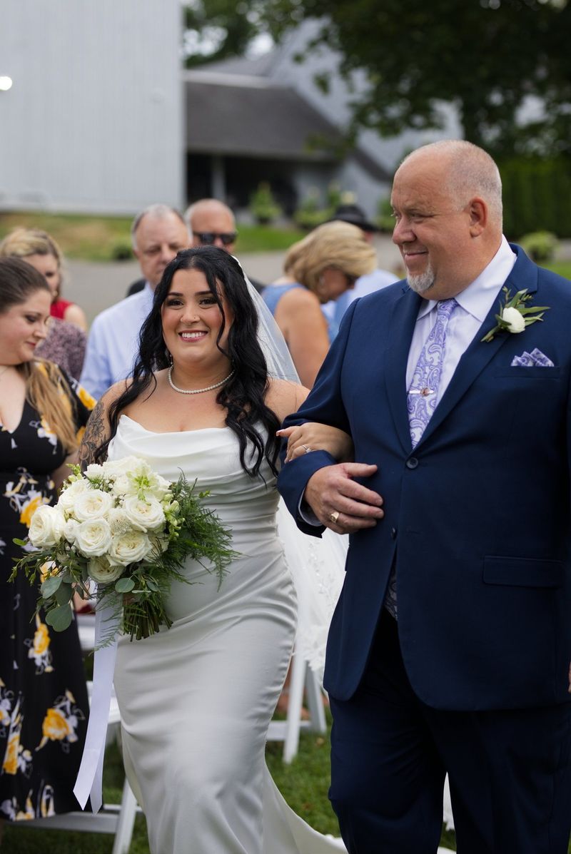 Sadie smiles as she walks down the outdoor aisle with a family member