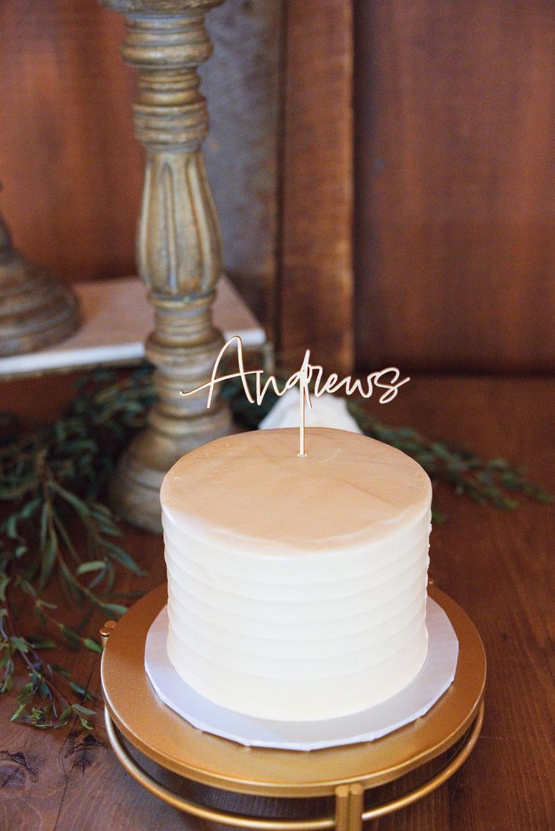 A white wedding cake with an Andrews topper against the barn’s wood interior