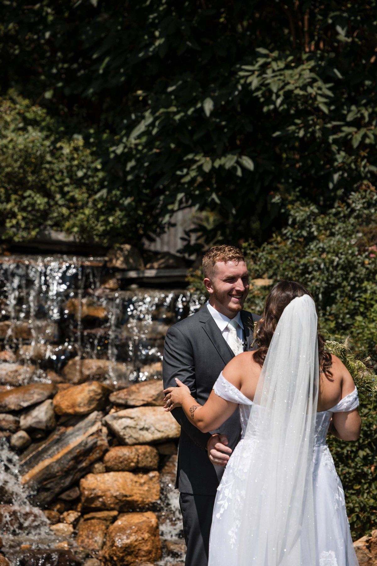 Tommy smiles as Sophia approaches him beside the garden waterfall