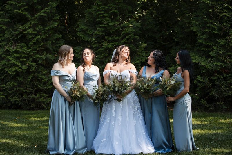 Sophia laughs with the bridesmaids while they hold bouquets on the lawn