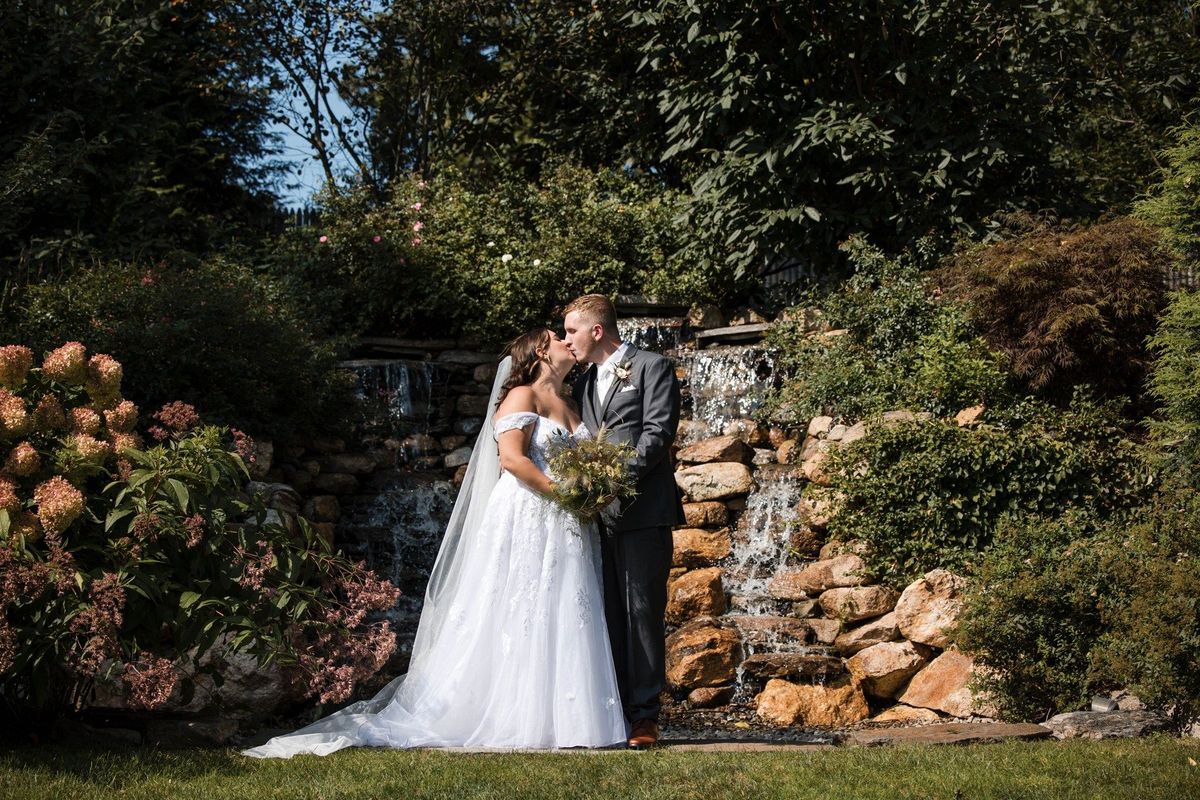 Sophia and Tommy kiss beside the rock waterfall surrounded by garden planting