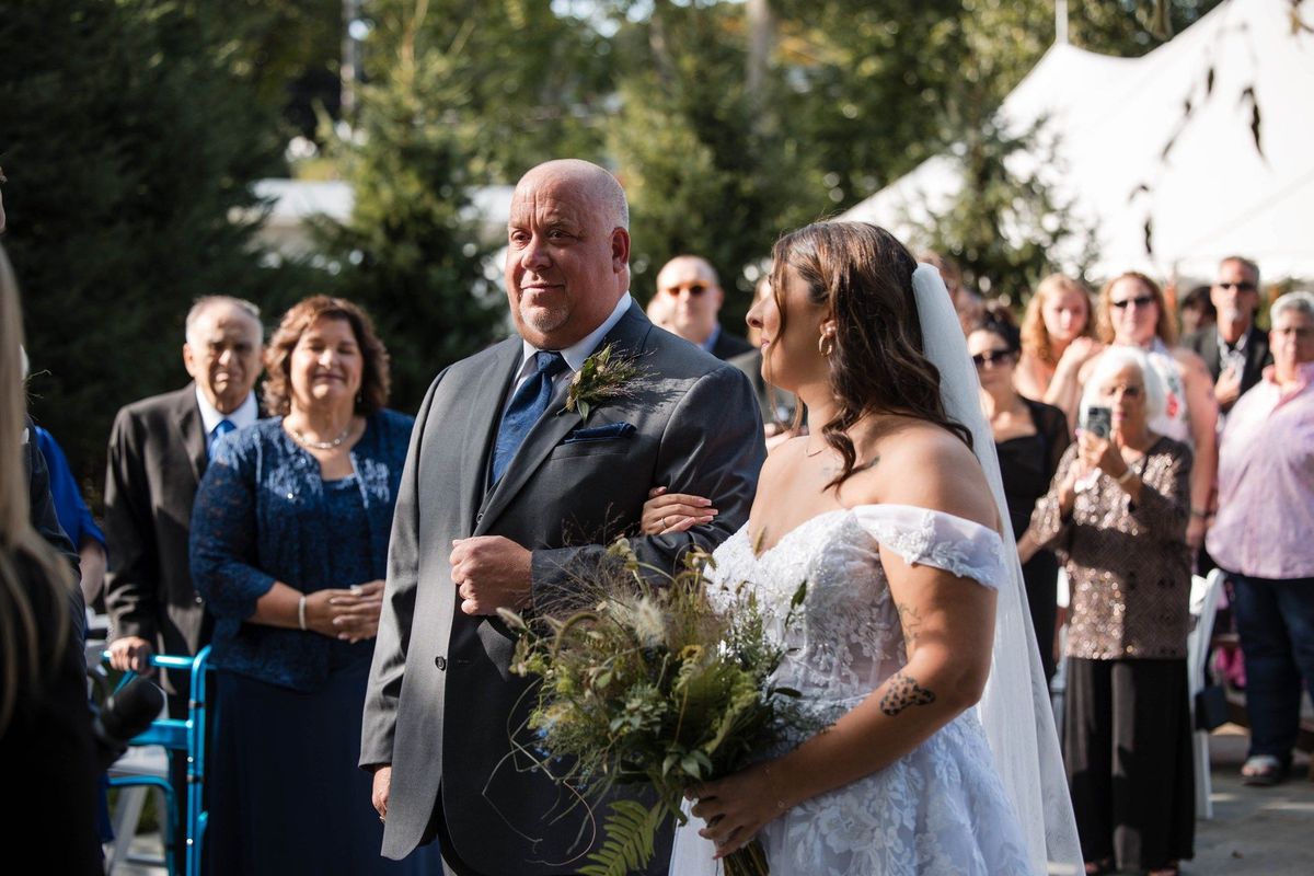 Sophia walks down the garden aisle beside a companion as guests look on