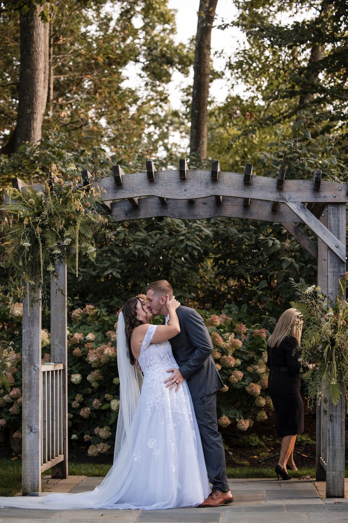 Sophia and Tommy kiss beneath the wooden ceremony arbor