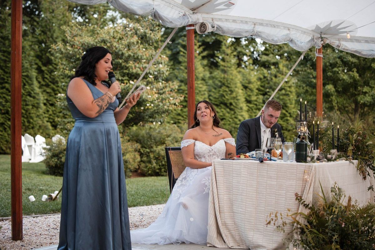 A speaker addresses Sophia and Tommy as the couple laugh at their reception table