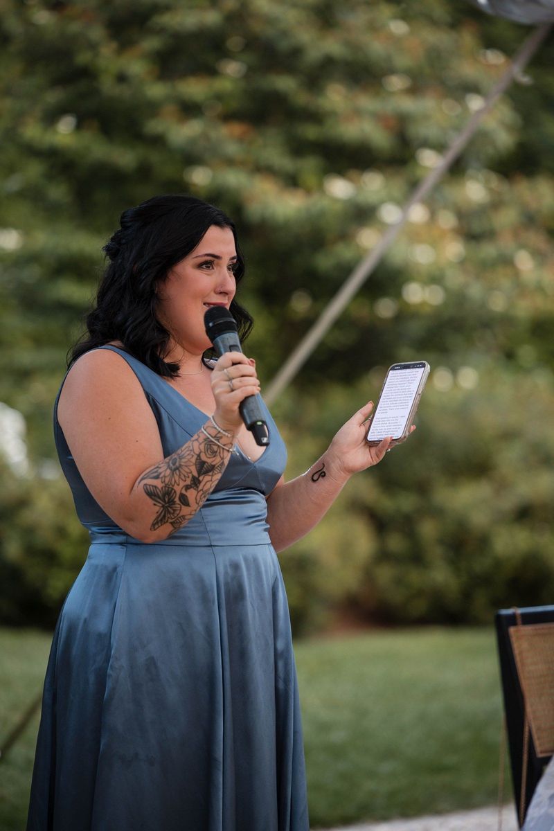 A wedding guest speaks into a microphone while holding a phone during speeches
