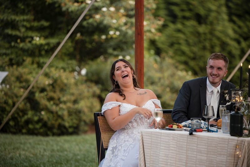 Sophia laughs with her head tilted back while Tommy smiles at the reception table