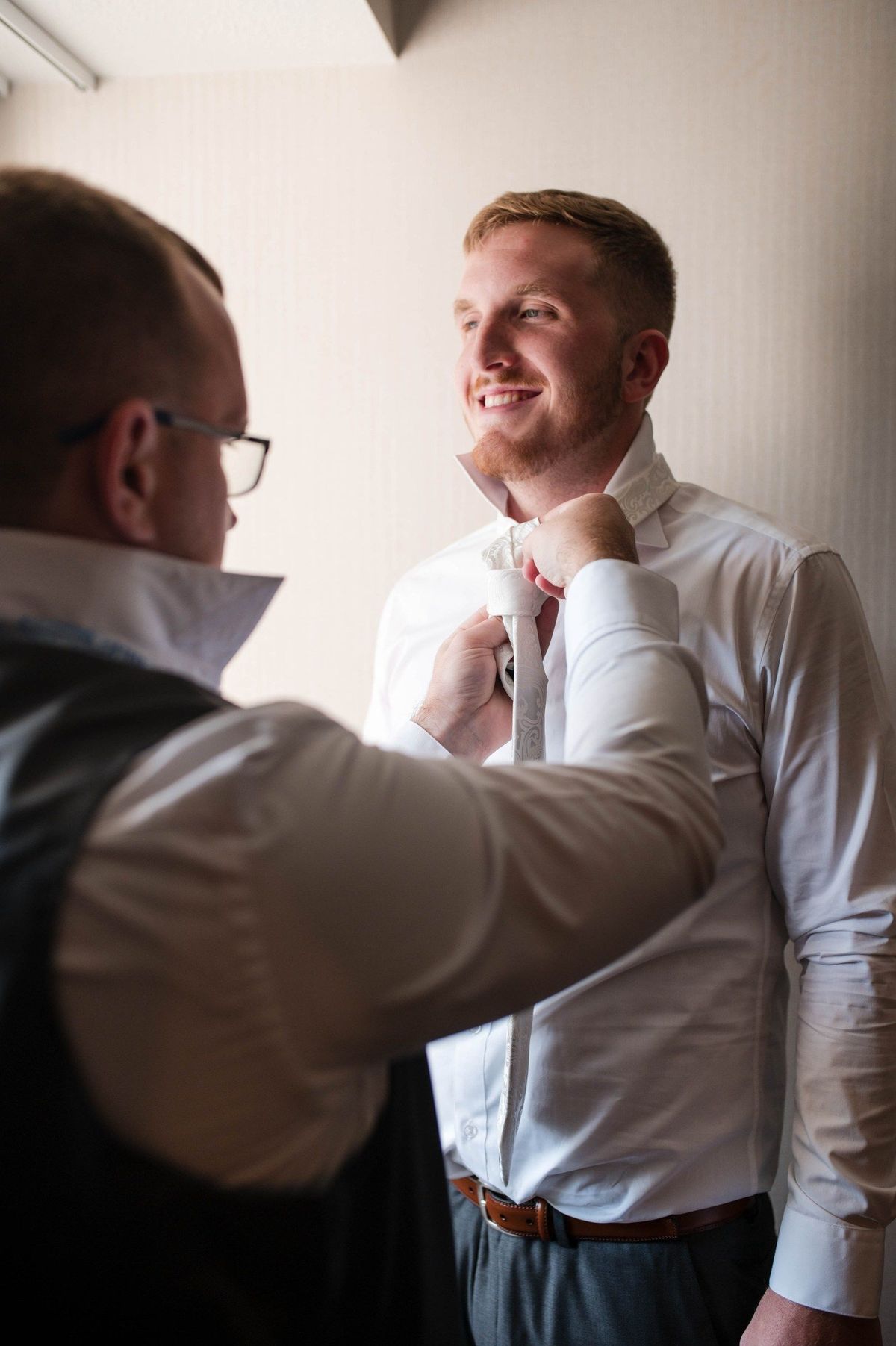 A companion adjusts Tommy’s tie beside a window